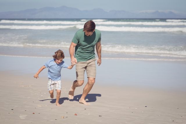 Father and son enjoying a sunny day at the beach, running along the shoreline. Perfect for themes of family bonding, summer vacations, outdoor activities, and happy childhood moments.