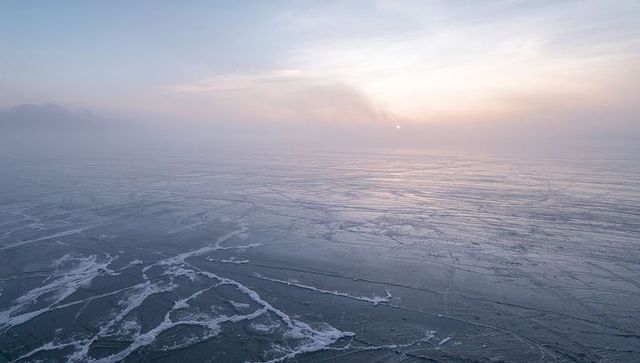 Stretching frozen lake cracking with ice ribbons and misty dawn pastel light haze