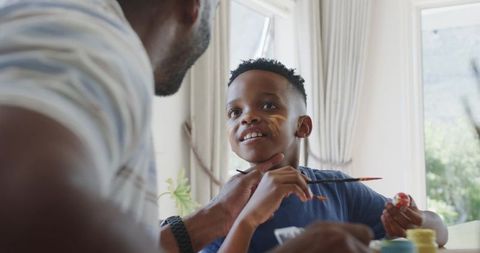 African american father and son painting at sunlit home table, creative family bonding