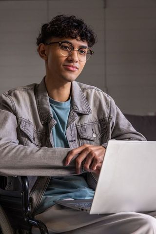 Young asian man working on laptop in modern home office wearing denim jacket and glasses