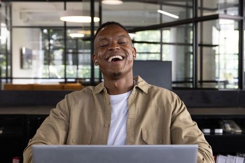 Laughing African American Man in Modern Office with Laptop