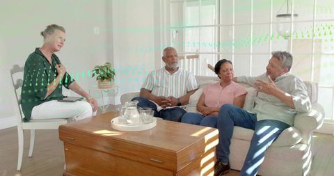 Facilitator leading sunlit living room conversation with mature couple, tablet and tray