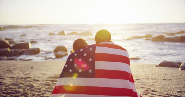 Couple wrapped in American flag sitting on beach at sunset - Download Free Stock Images Pikwizard.com