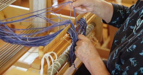 Senior woman skillfully operating handloom with blue thread