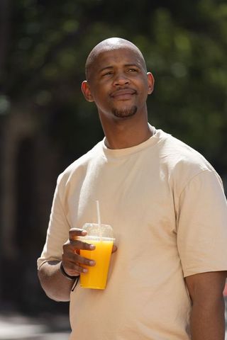 African american man standing holding orange juice cup enjoying sunny park portrait