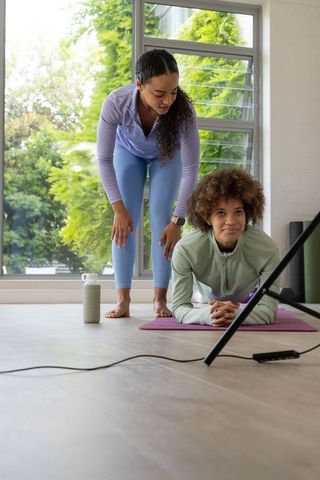 African american trainer guiding woman planking during home workout by window greenery
