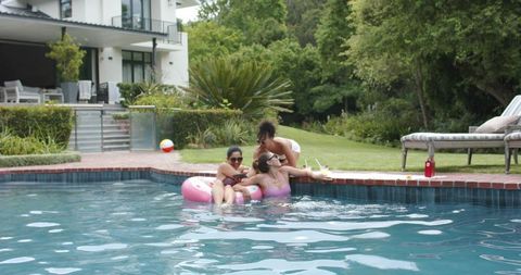 Diverse friends laughing and relaxing on pink pool float at luxury backyard summer pool