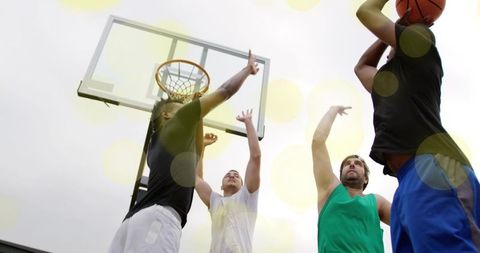 Four men jumping and contesting basketball shot on outdoor neighborhood court with hoop
