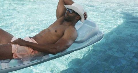 Relaxing man on inflatable pool lounger wearing sunhat and sunglasses, summer resort