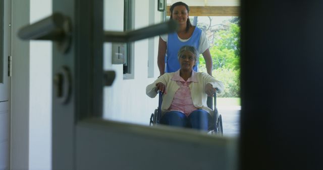 Senior woman in wheelchair being pushed by caregiver on outdoor patio. Suitable for healthcare services promotion, nursing home advertisements, and senior care resources.