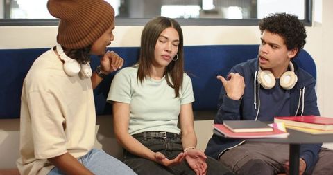 Young african friends debating in campus lounge with headphones and textbooks, collaboration