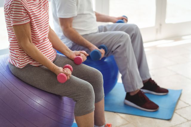 Senior couple exercising with dumbbells on exercise ball at home