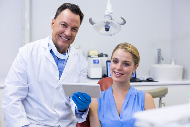 Dentist showing a female patient her dental x-ray on a tablet. Both are smiling, indicating a positive and reassuring environment. Ideal for use in healthcare, dental care, and technology in medicine promotions.