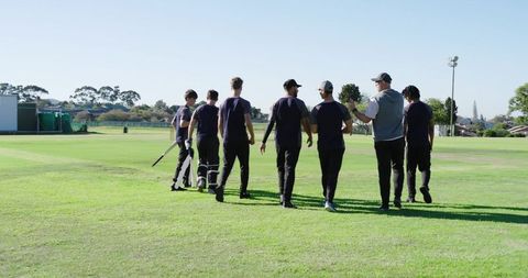 Cricket team walking off field with coach celebrating victory, diverse male players