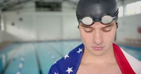 Male swimmer with flag goble near indoor pool displaying determination