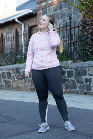 Pausing mid-walk, tucking hair in pink hoodie and leggings on urban sidewalk