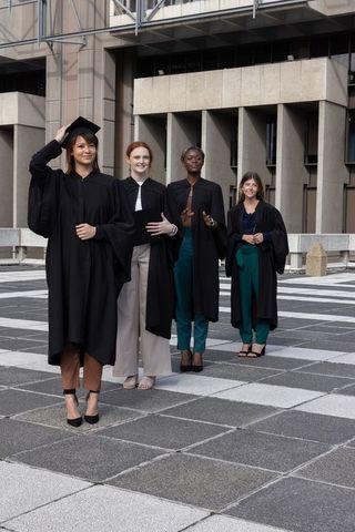 Diverse female graduates celebrating on university plaza wearing black gowns and mortarboards