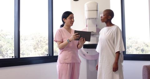 Technologist explaining mammography procedure to patient in gown beside mammography unit