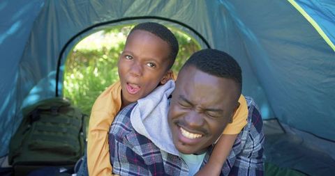 African american father and son playful piggyback camping in teal tent during daylight