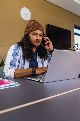 Young man multitasking on laptop while talking on phone in bright modern study space
