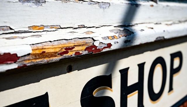 Peeling paint on weathered shop trim revealing multicolor undercoats and aged timber texture