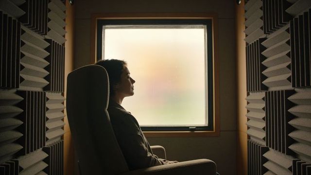 Sitting asian woman reflecting in acoustic studio booth with foam panels and armchair softly lit
