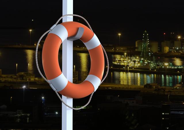 Life belt hanging on a pole with a cityscape and river in the background at night. The image highlights safety and emergency preparedness in an urban waterfront setting. Ideal for use in articles or advertisements related to maritime safety, urban security, or nighttime cityscapes.