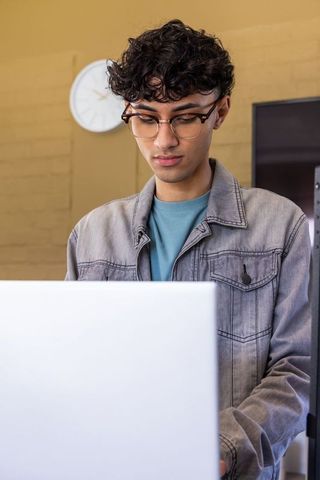 Focused asian teen studying on laptop wearing glasses and denim jacket