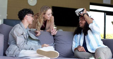 Young friends exploring virtual reality together on modern lounge sofa, tech hangout