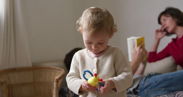 Curious Toddler Exploring Toy While Mother Reads Book in Background - Download Free Stock Images Pikwizard.com