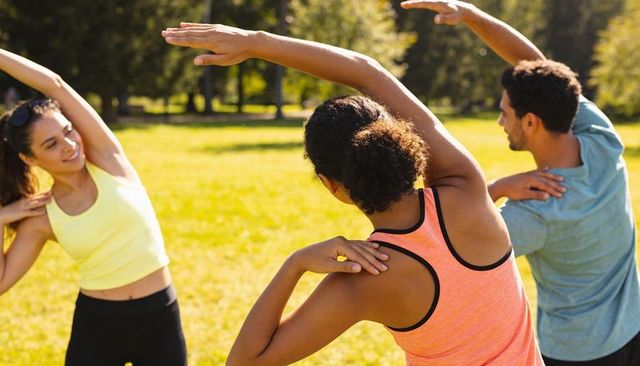 Trainer leading group outdoor side-stretch class in sunlit park