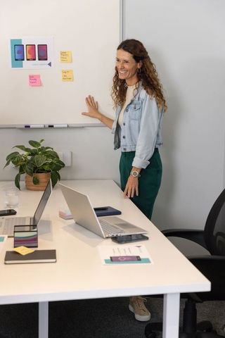Mature woman presenting mobile app mockup on whiteboard during collaborative ux workshop