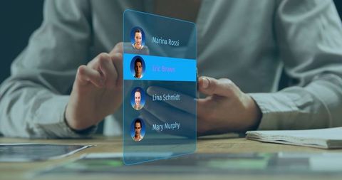 Holding phone at wooden desk tapping holographic contact list interface with avatars