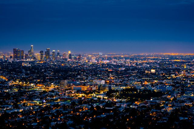 Vibrant view of Los Angeles skyline at dusk, featuring illuminated city lights and a sprawling urban landscape. Perfect for use in travel brochures, real estate promotions, urban planning presentations, and advertising for the city of Los Angeles. Highlights the beauty of the city and its dynamic energy at twilight.