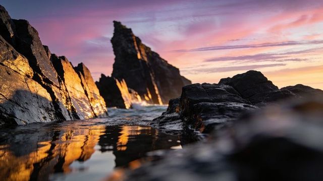 Golden tide pool reflections at sunset with pointed sea stack and rocky foreground