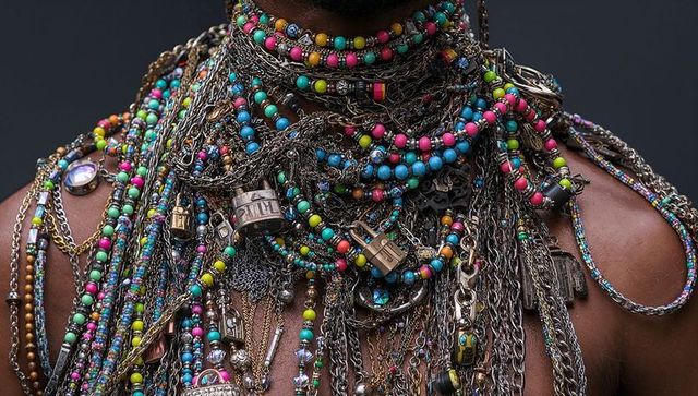 Male torso wearing layered metal chains and neon bead necklaces with padlocks