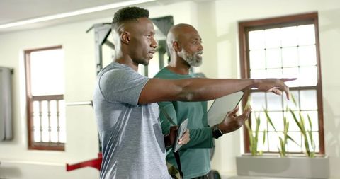 African american personal trainer guiding client through exercise technique in bright gym