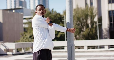 African american man stretching shoulder on rooftop using pole wearing smartwatch