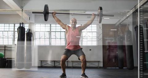 Mid-adult man performing overhead squat with Olympic barbell in sunlit industrial gym