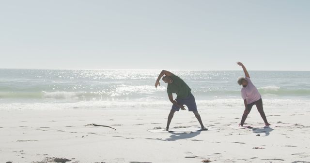 Senior couple performing stretching exercises on a sunny beach by the ocean. Ideal for use in advertisements and articles related to senior fitness, health and wellness, active aging, outdoor activities, and promoting a healthy lifestyle for older adults.