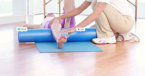 Personal trainer guiding client through foam roller mobility exercise in sunlit studio
