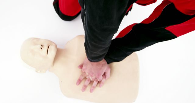 An emergency responder wearing a red and black uniform demonstrating proper chest compressions on a CPR training mannequin. Useful for illustrating CPR techniques, first aid training courses, healthcare and safety instruction, and educational material for emergency preparedness.