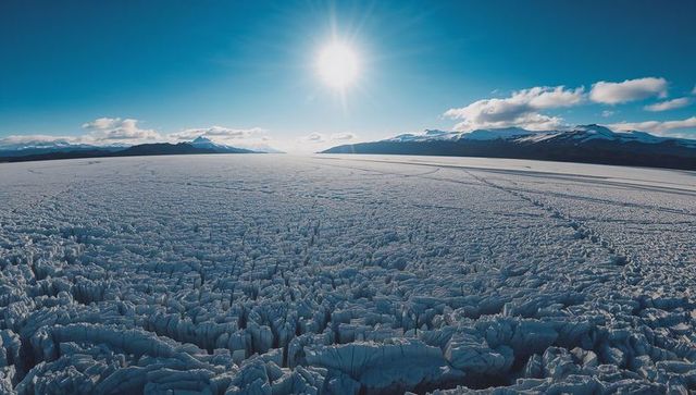 Sunlit Glacier Field with Jagged Ice Pinnacles, Crevasses and Distant Snowy Mountains