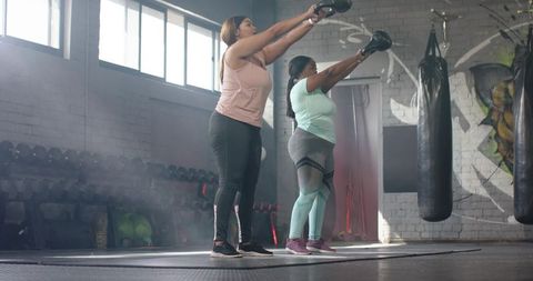 Multiracial women lifting kettlebells in urban gym strength and body-positive training