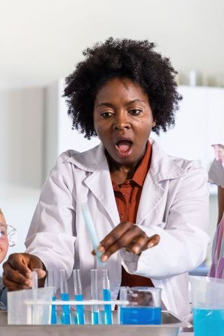 African-american woman showing surprise pipetting blue liquids in classroom science experiment