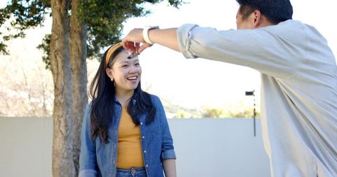 Asian couple outdoors, man adjusting yellow headband, woman smiling in denim jacket