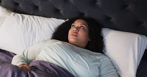 Middle-aged woman lying in bed gazing upward, contemplative sleepless night