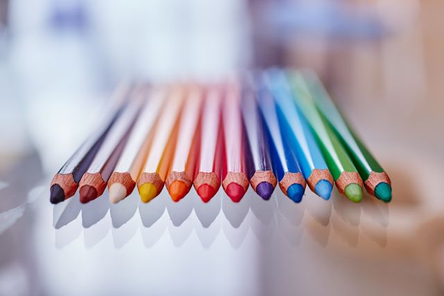 Colorful pencils neatly aligned on a reflective surface. Ideal for use in creative projects, education materials, school stationery advertisements, or office supply promotions. Emphasizes organization, creativity, and vibrancy, suitable for websites, blogs, and advertisements highlighting artistic tools and educational resources.