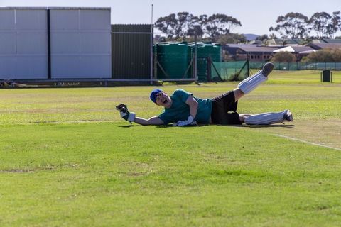 Diving fielder sliding near boundary during sunny community cricket match