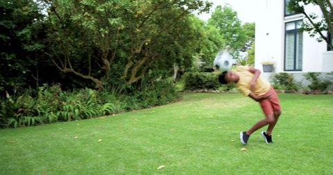African american teen heading soccer ball on backyard lawn showing athletic skill